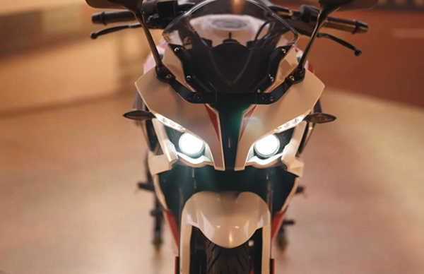 Front view of a BAJAJ PULSAR RS200 motorcycle brightly lit with headlights on in an indoor setting.